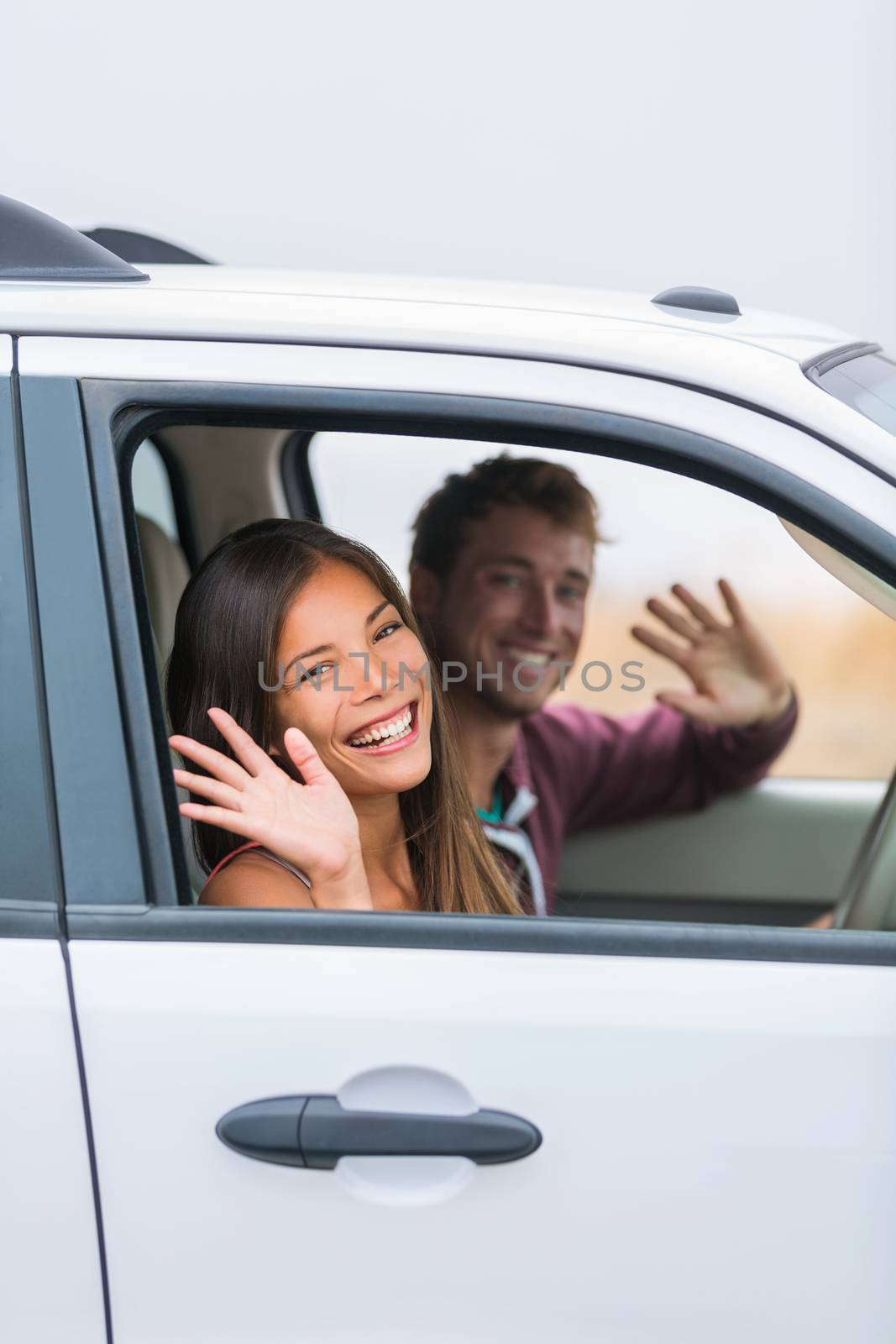 Happy multiracial couple leaving for road trip on summer vacation holiday. Young people driving car to travel destination waving goodbye by Maridav