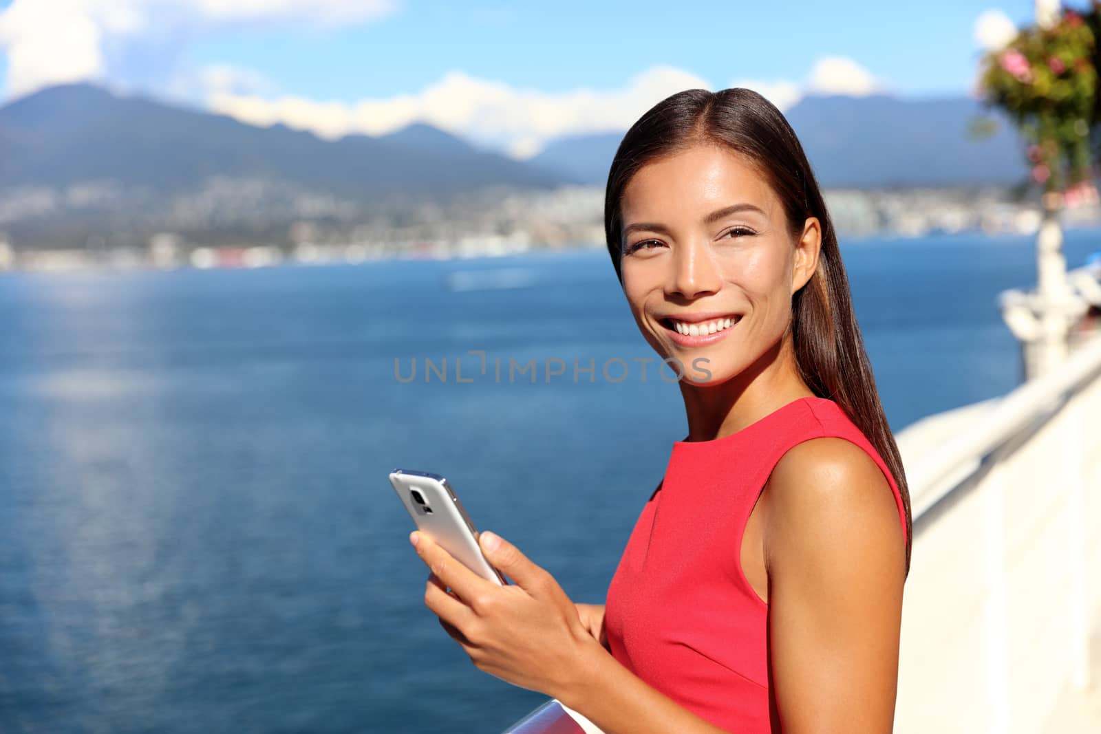 Happy asian woman using phone app in vancouver city harbour on summer day. Beautiful landscape of canadian nature river and mountains. Businesswoman on smartphone lifestyle.