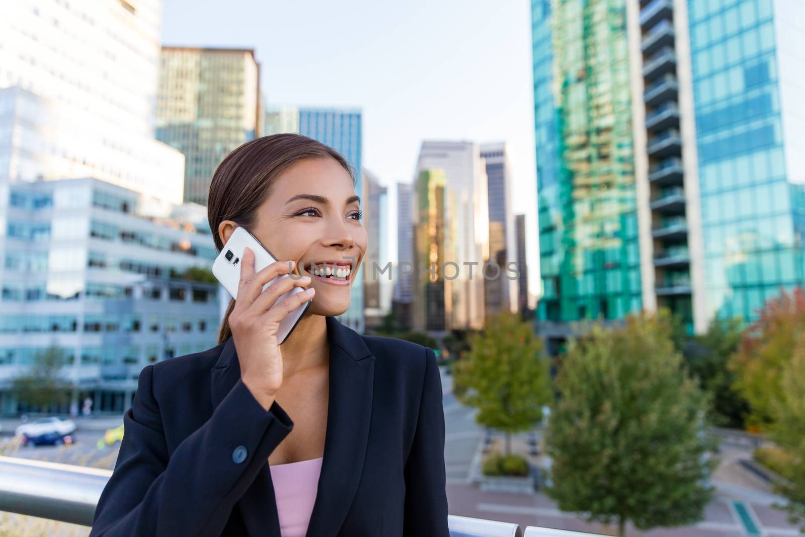 Smart phone woman calling on mobile phone in city business district. Confident young business woman talking on smartphone smiling happy wearing suit jacket outdoors. Urban female professional in 20s.
