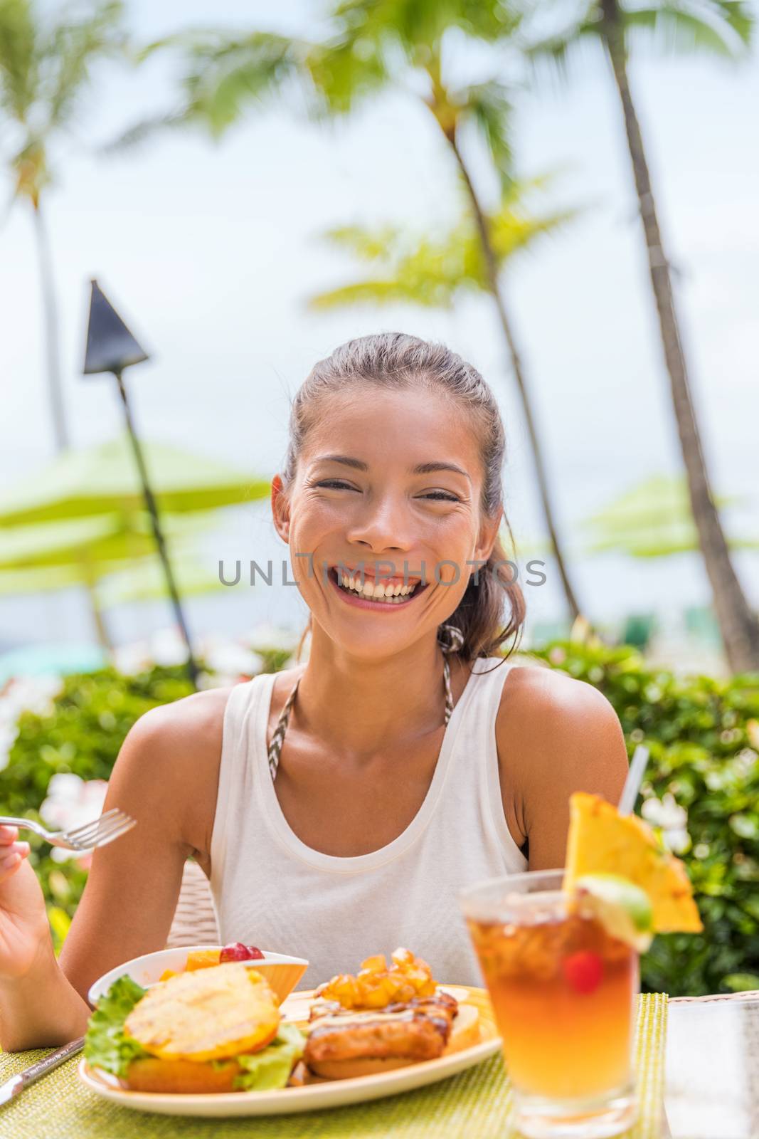 Happy woman at restaurant eating Hawaii burger with pineapple and karaage fried chicken. Hawaiian japanese fusion food. Asian girl at hotel restaurant table during summer travel vacation by Maridav