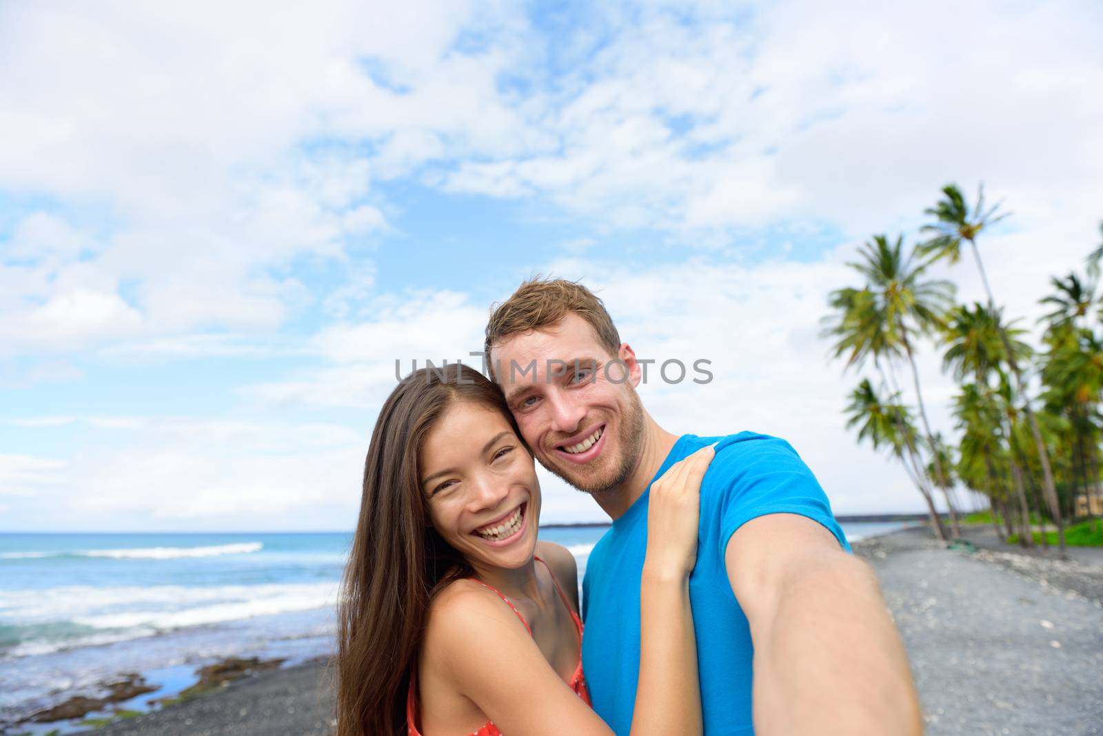 Selfie couple on Hawaii beach holiday taking pictures with smartphone on summer vacations in Big island, Hawaii. Travel destination. People having fun vlogging on social media on hawaiian holidays.