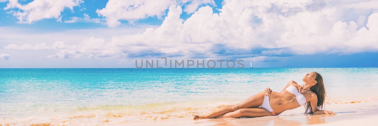 Beach paradise sexy bikini woman lying down on sand relaxing sun tanning in tropical caribbean travel destination for summer vacation. Panoramic banner landscape with copy space on blue ocean by Maridav
