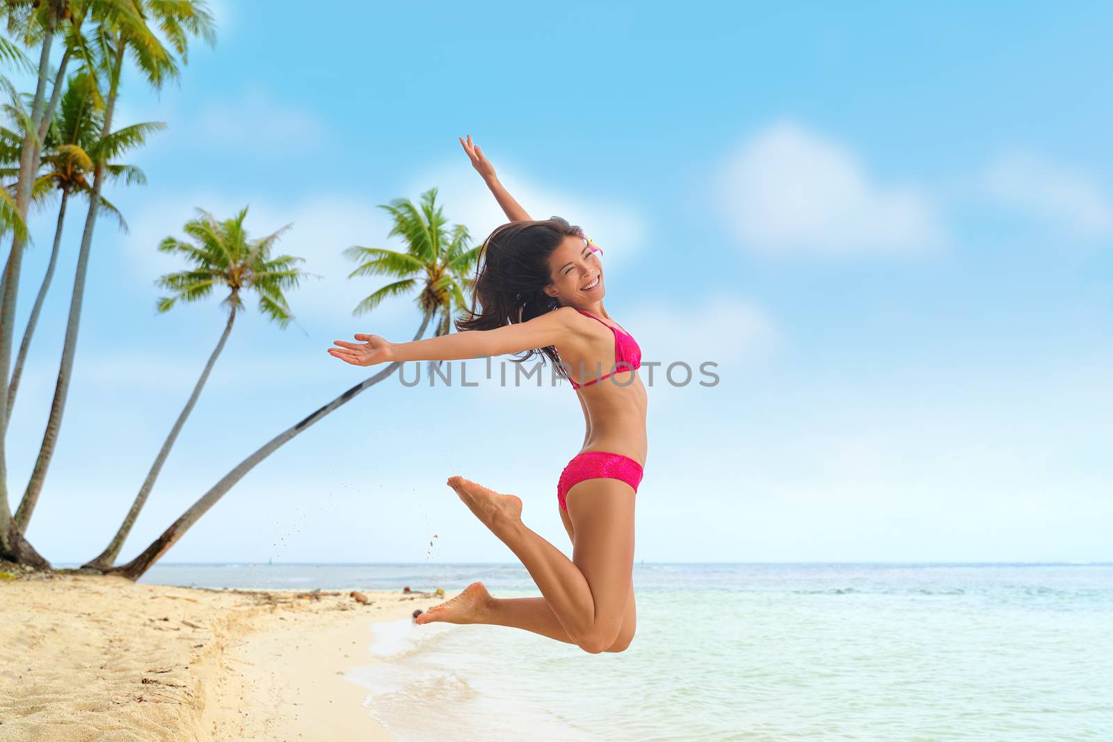Beach fun summer vacation under the sun joyful happy bikini woman jumping of joy on Tahiti luxury travel destination. Asian girl happiness jump.
