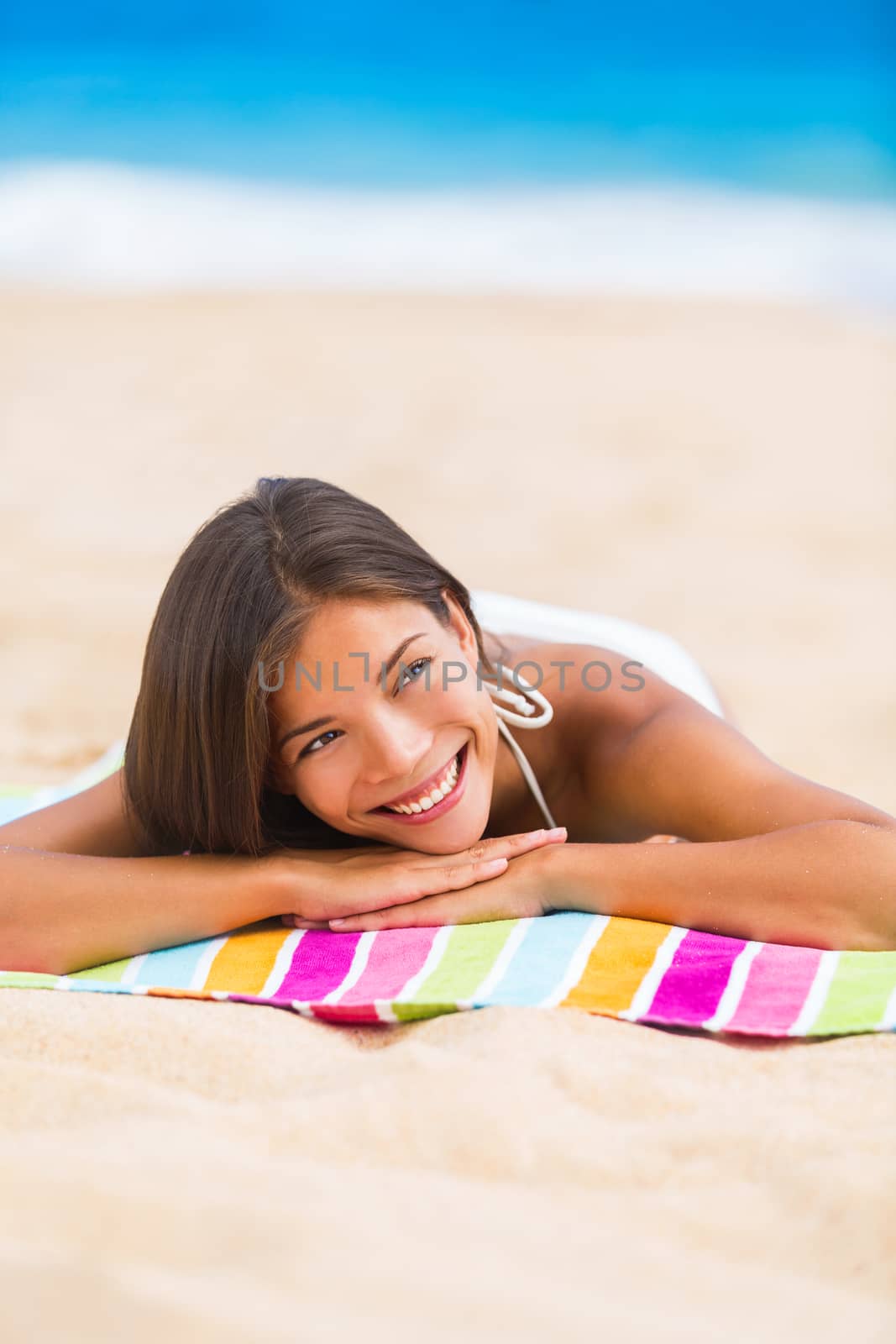 Beach woman thinking looking up at copyspace. Multiracial Asian Chinese / Caucasian female girl relaxing on beach towel smiling happy.