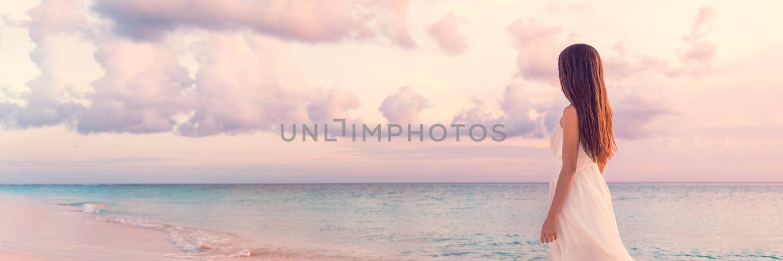 Peaceful vacation paradise woman walking on sunset beach with pastel colors sky and ocean for tranquility and serenity banner. Girl in white wedding dress relaxing on luxury tropical summer getaway.