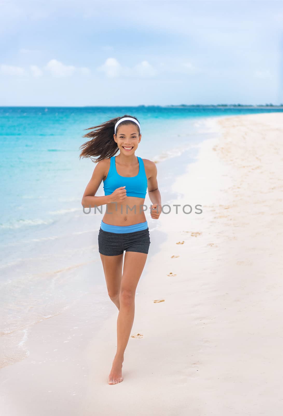 Running on beach fitness runner sportswear woman. happy Asian fit girl training jogging in blue sports bra and shorts on summer tropical vacation destination. Healthy active lifestyle on travel.