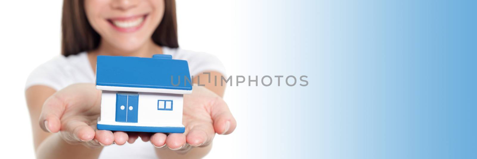 Real estate house banner with blue copy space panorama. Woman smiling showing miniature toy home holding hands for home insurance protection concept.