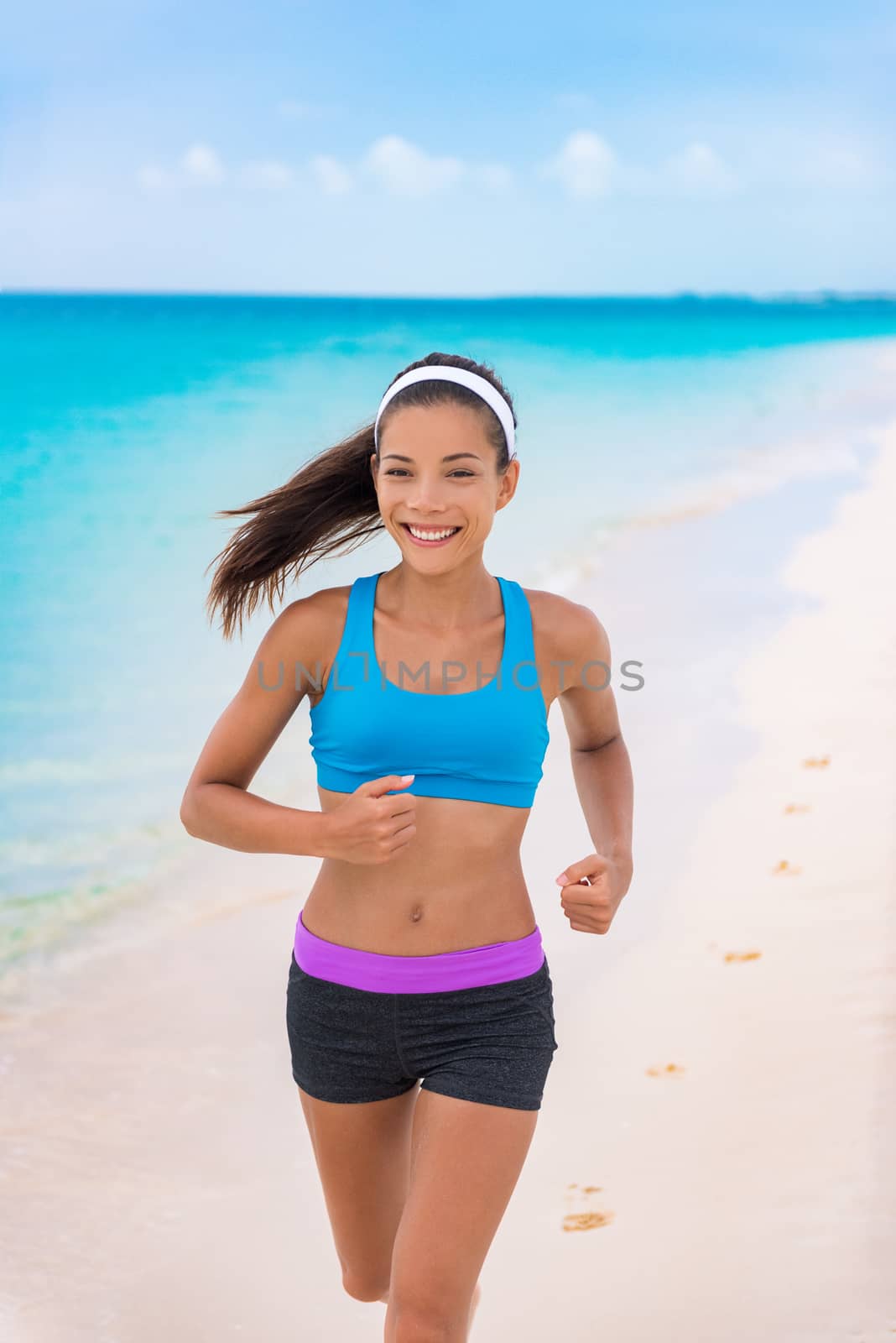 Fitness girl running on beach in fashion activewear clothes. happy Asian woman jogging with blue sports bra and shorts on morning training outside. Summer travel.