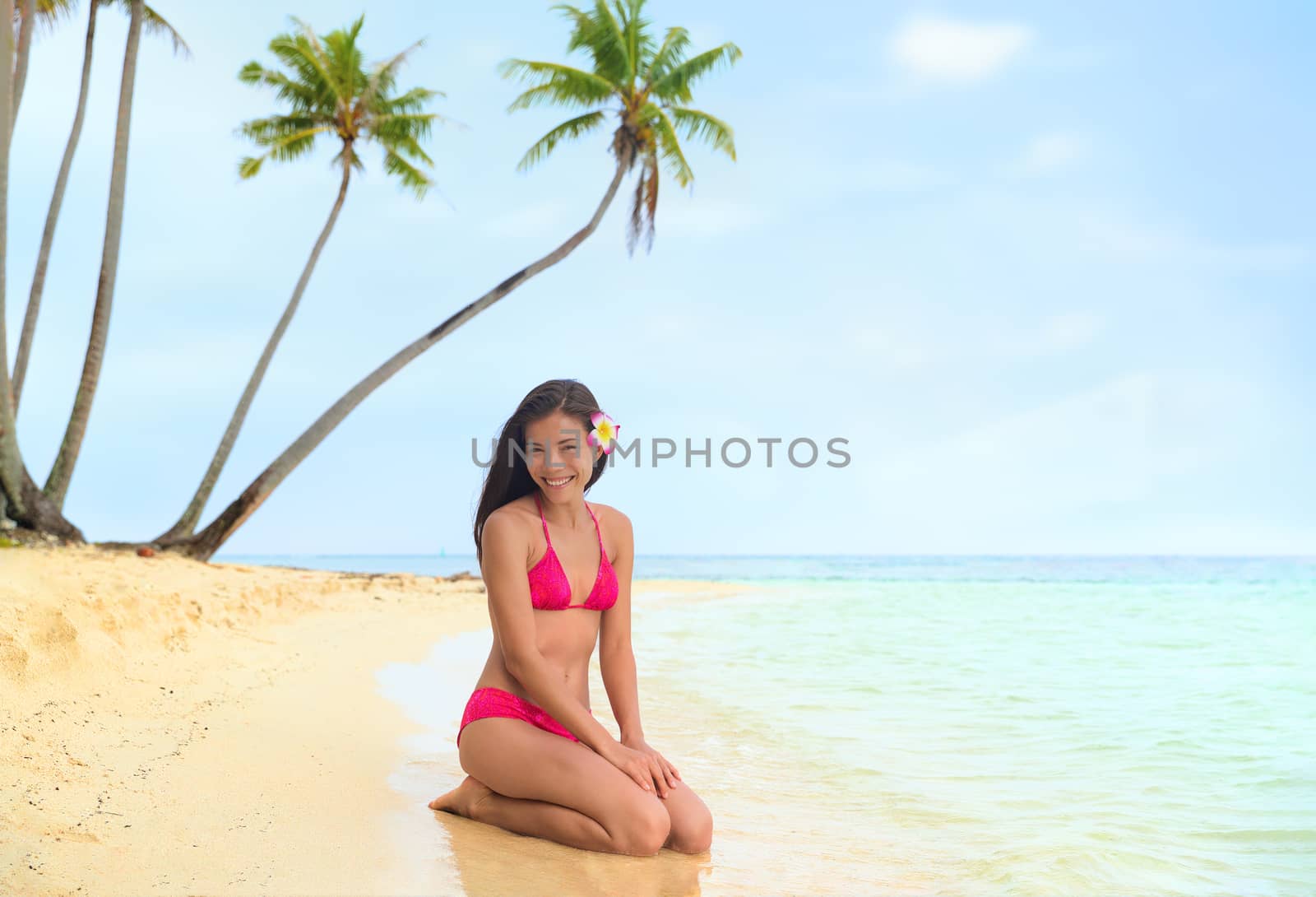 Beautiful bikini model on Tahiti luxury travel vacation island posing in red swimwear relaxing on sand. Asian woman happy smiling with tropical paradise ocean background.