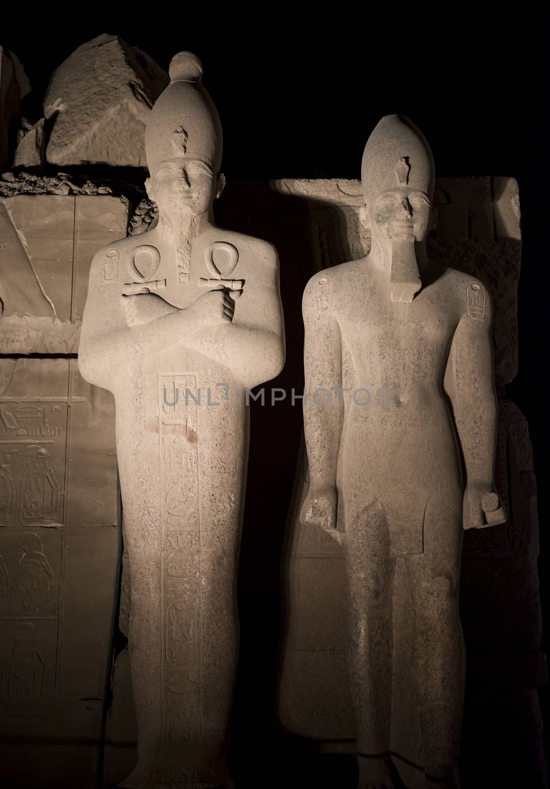 Tall stone ancient egyptian statues at Karnak Temple in Luxor lit up during night on black sky background