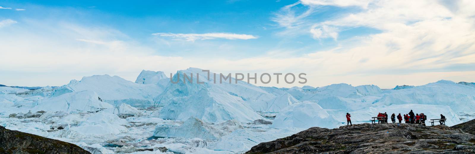 Icebergs in arctic landscape nature with travel tourists in Greenland. People looking at amazing view of Greenland Icebergs in Ilulissat icefjord affected by climate change and global warming.