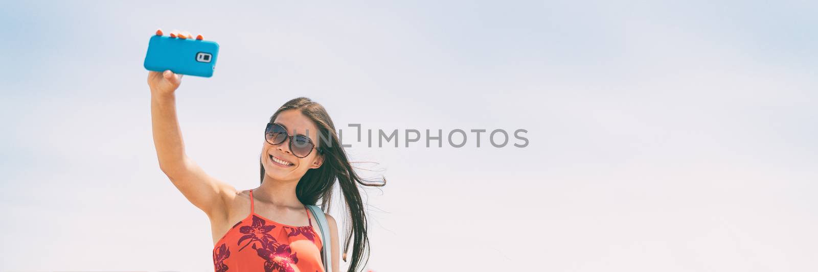 Selfie picture with phone woman tourist holding cellphone taking self-portrait photo on summer holiday. Young people lifestyle banner panorama with copy space on blue sky background.