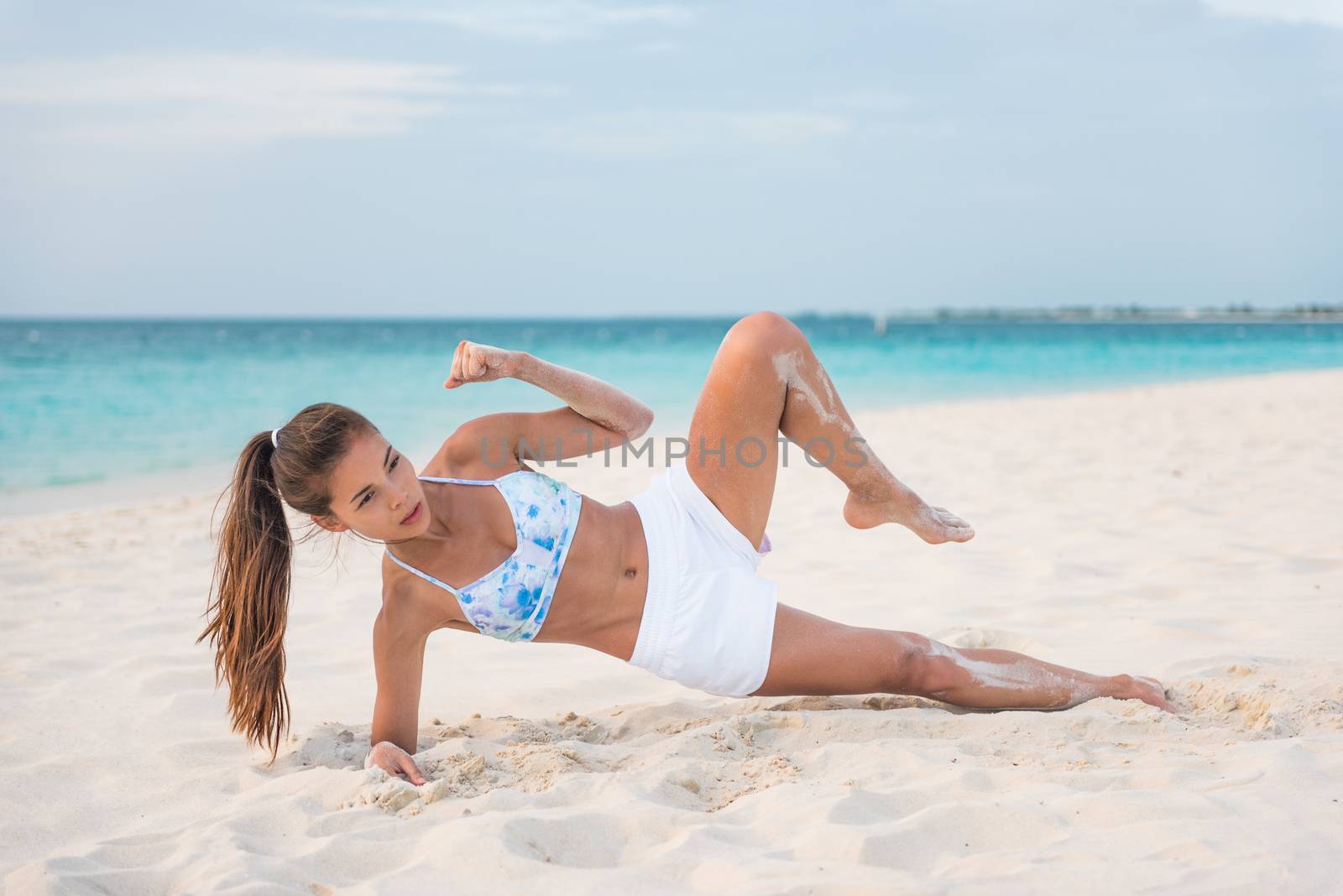 How to do a Side Plank Crunch fitness instruction demonstration physical trainer on beach training obliques stomach muscles doing core body training. Fit girl exercising doing abs exercise.