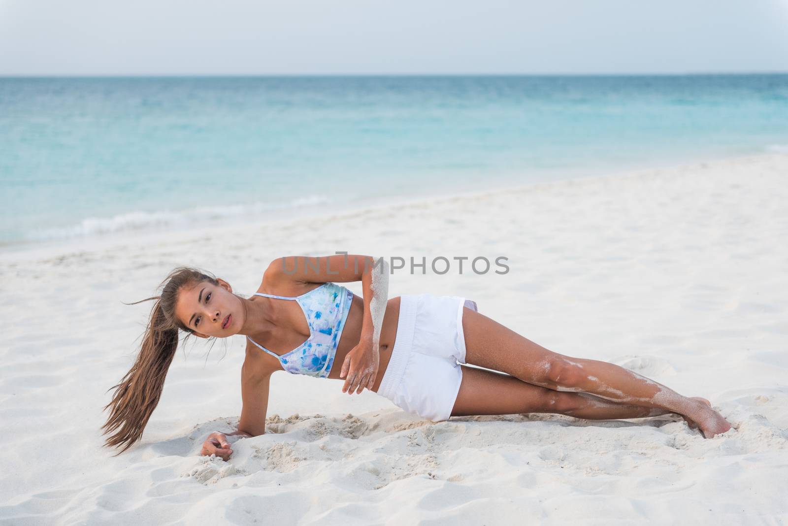 Planking exercise side plank with twist yoga fitness girl training obliques muscles for stomach toning on sunset beach. Active woman travel lifestyle.