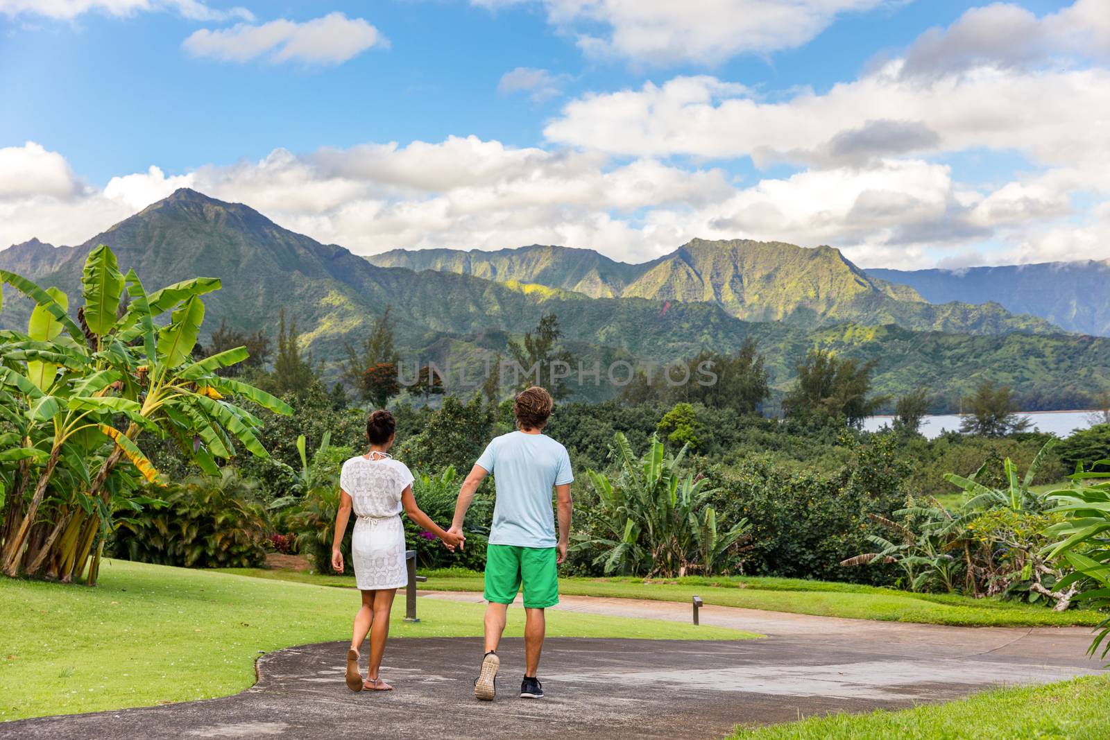 Couple tourists walking on Hawaii vacation. Two young people relaxing in Hanalei Bay resort in Kauai, Hawaii travel beach destination with Kauai mountains in the background.