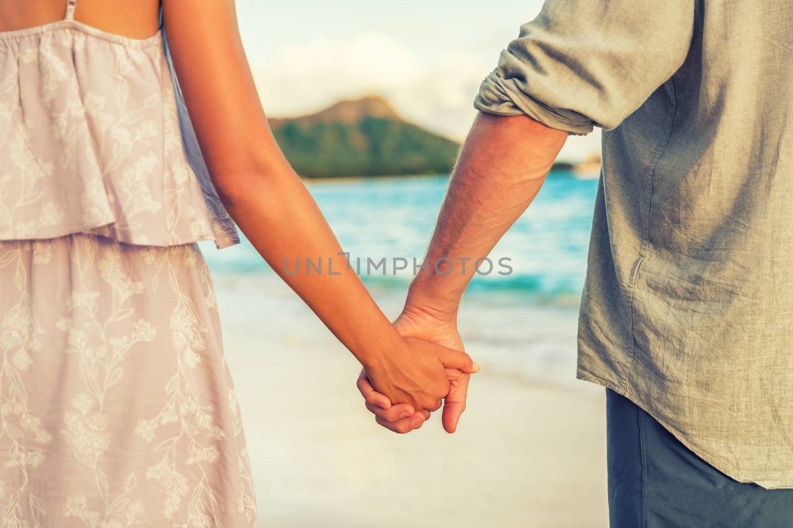 Couple holding hands relaxing on Hawaii beach in sunset. Young people in love in Waikiki travel Honolulu, Hawaii.