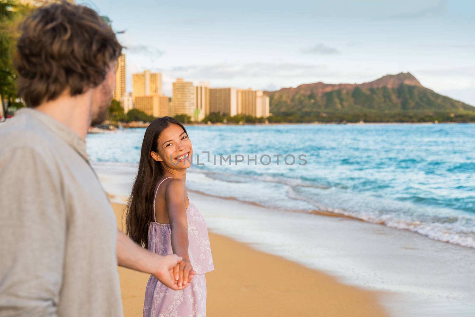 Couple relaxing holding hands having fun on Waikiki beach Hawaii vacation. Happy tourists people in love walking at sunset on popular travel destination in Honolulu, Oahu, Hawaii by Maridav