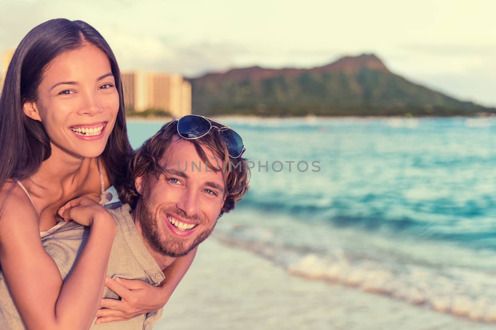 Happy interracial couple, woman piggybacking on man on Waikiki beach with Diamond Head Mountain landscape. Healthy people portrait, Honolulu, Hawaii. Travel holidays destination by Maridav