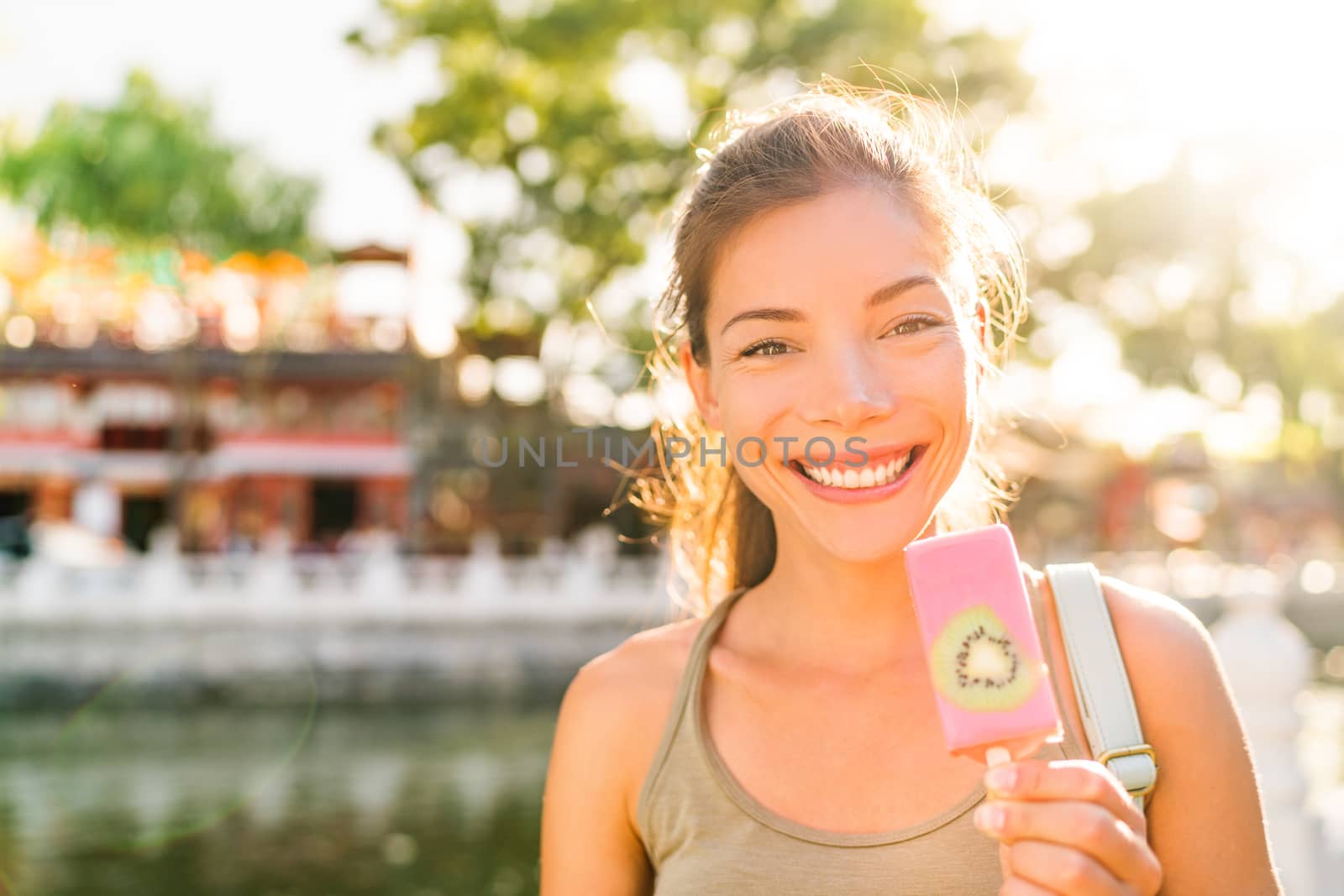 Asian tourist woman eating ice cream pop stick in Beijing city, China. Asia summer travel vacation. Healthy foodie girl eating frozen fruit snack near Houhai lake. Popular tourism destination.
