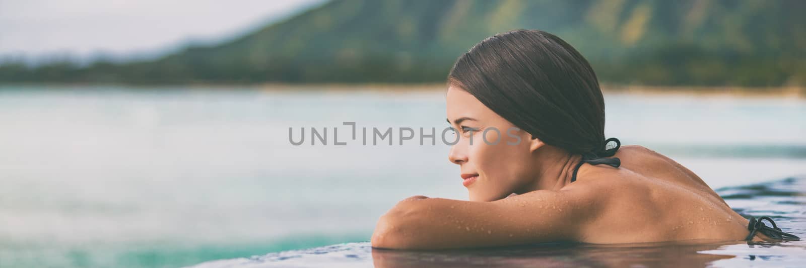 Luxury vacation woman relaxing in infinity swimming pool on summer travel at beach resort. Asian girl tourist on wellness spa relaxation outside in nature landscape banner panorama by Maridav