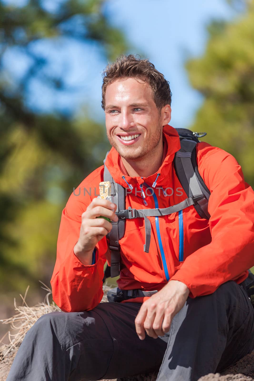 Hiker man healthy outdoor lifestyle eating muesli bar during hike on mountain hiking. Happy people eat granola cereal bar snack living active lifestyle in nature.