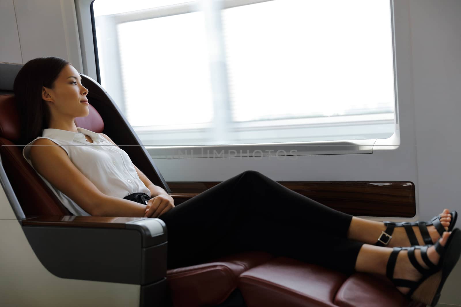 Elegant lady relaxing in comfortable first class seat with more legroom in train during travel. Asian woman lying down enjoying transport to urban city destination.