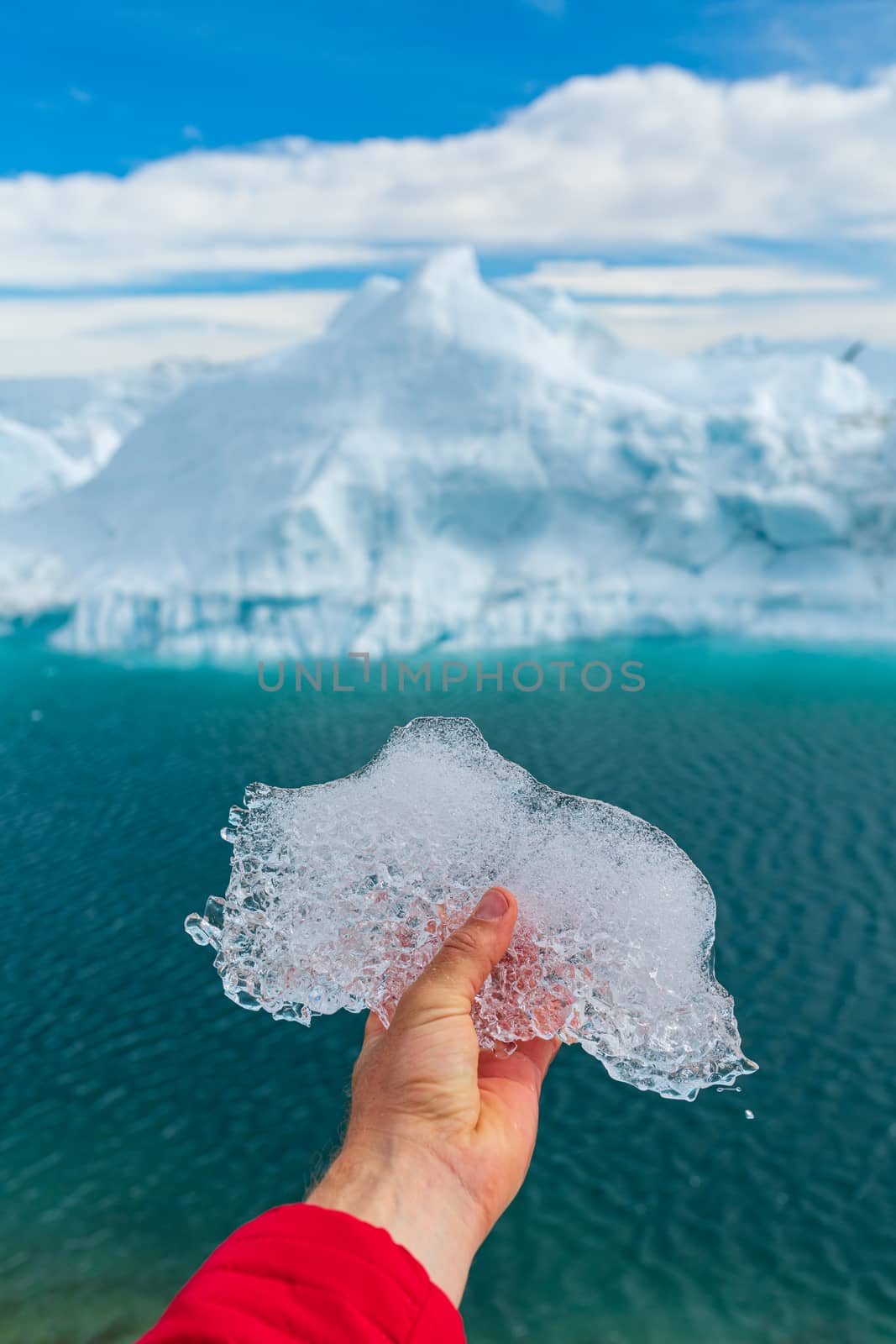 Save the climate! Global warming, climate change and Environmental protection concept with icebergs on Greenland. Hand holding melting ice in front of giant iceberg in Ilulissat icefjord on Greenland.