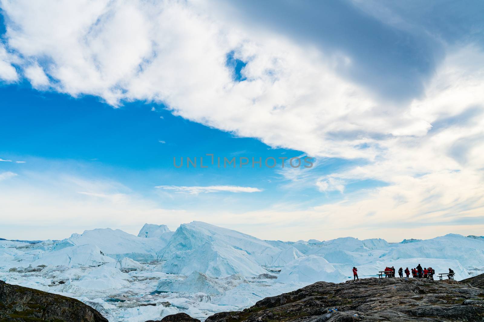Icebergs in arctic landscape nature with travel tourists in Greenland. People looking at amazing view of Greenland Icebergs in Ilulissat icefjord affected by climate change and global warming.