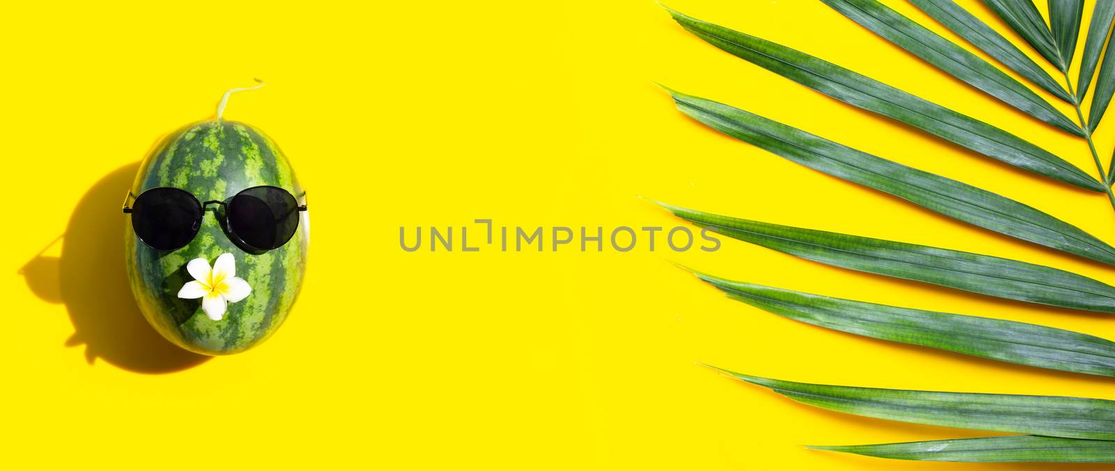 Watermelon with sunglasses and tropical palm leaves on yellow background. Enjoy summer holiday concept.