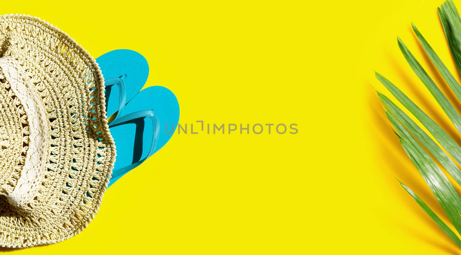 Summer hat with blue flip flops and tropical palm leaves on blue background. Copy space