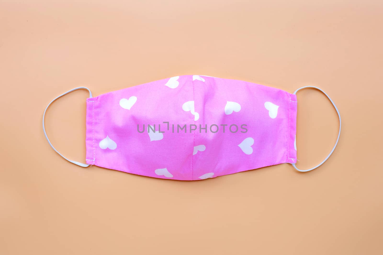 Handmade pink cloth mask with white heart shape on orange background. Top view