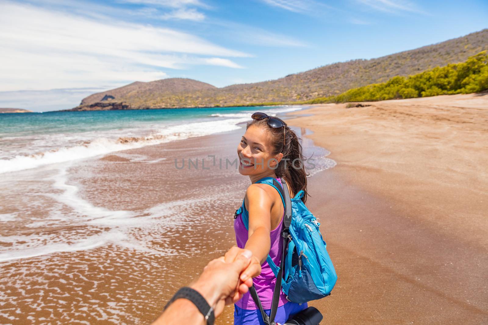 Galapagos tourist couple holding hands in follow me pose having fun on travel on Espumilla Beach, Santiago Island, Galapagos Islands, Ecuador. People on Cruise ship excursion.