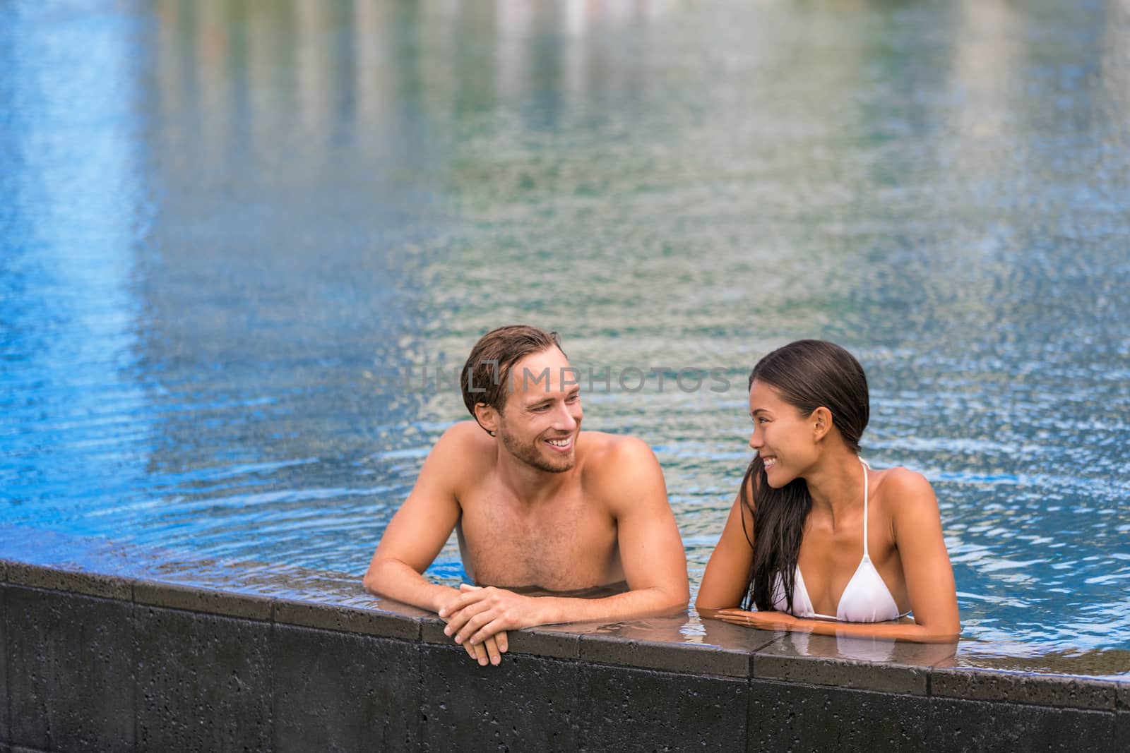 Pool couple relaxing on luxury resort travel holiday swimming in infinity pool at tropical villa hotel by Maridav