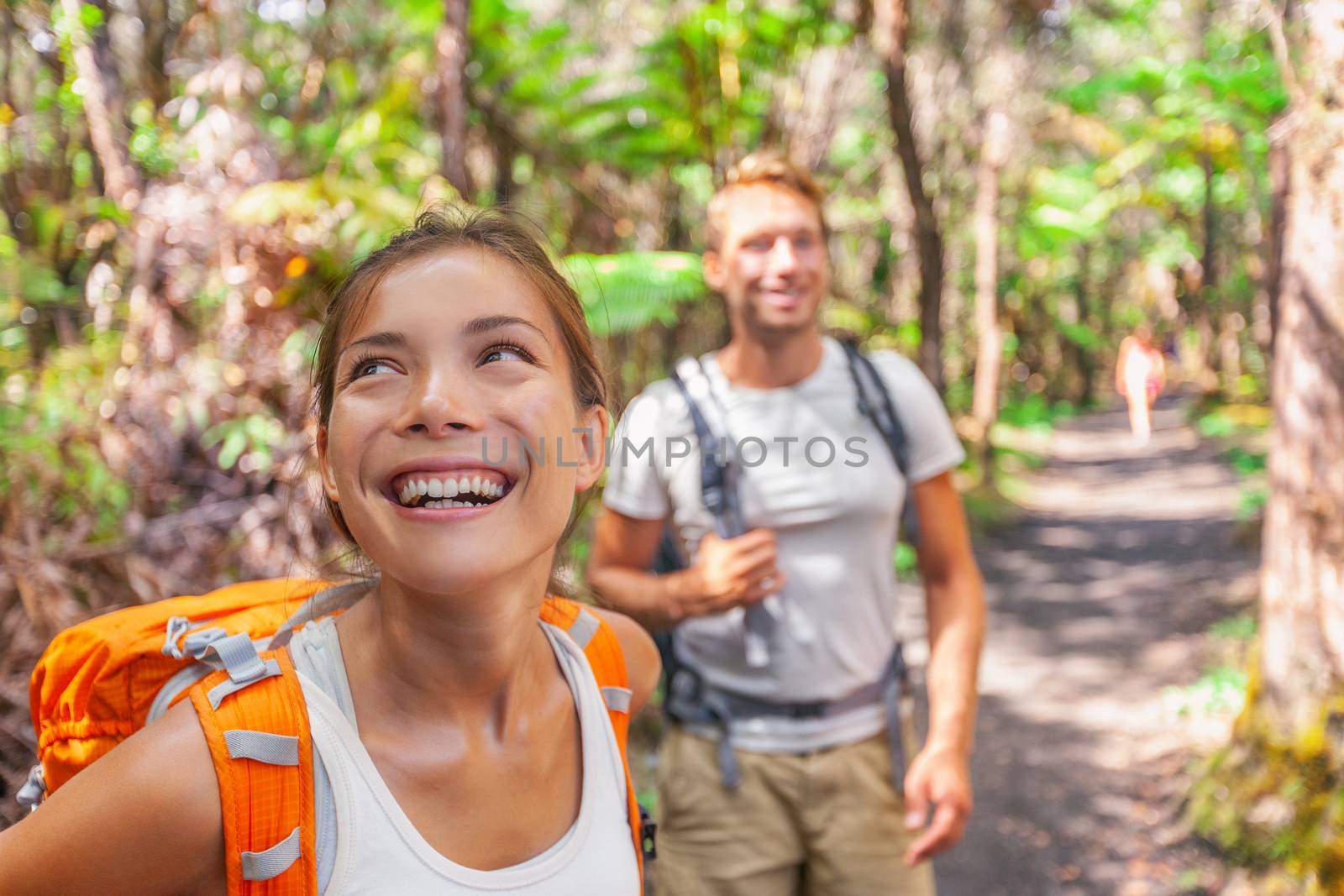 Hiking couple on travel hike outdoor trekking - young active people lifestyle camping with bags in forest. Smiling happy Asian woman enjoying walk in woods with friend.