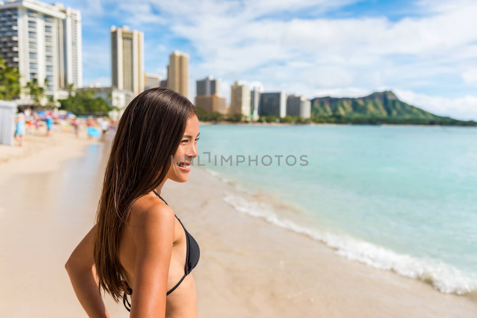 Happy Asian bikini woman enjoying holidays on Waikiki beach in Honolulu city, Oahu, with diamond head mountain landscape in the background. Multiracial girl sunbathing on Hawaii summer vacation.