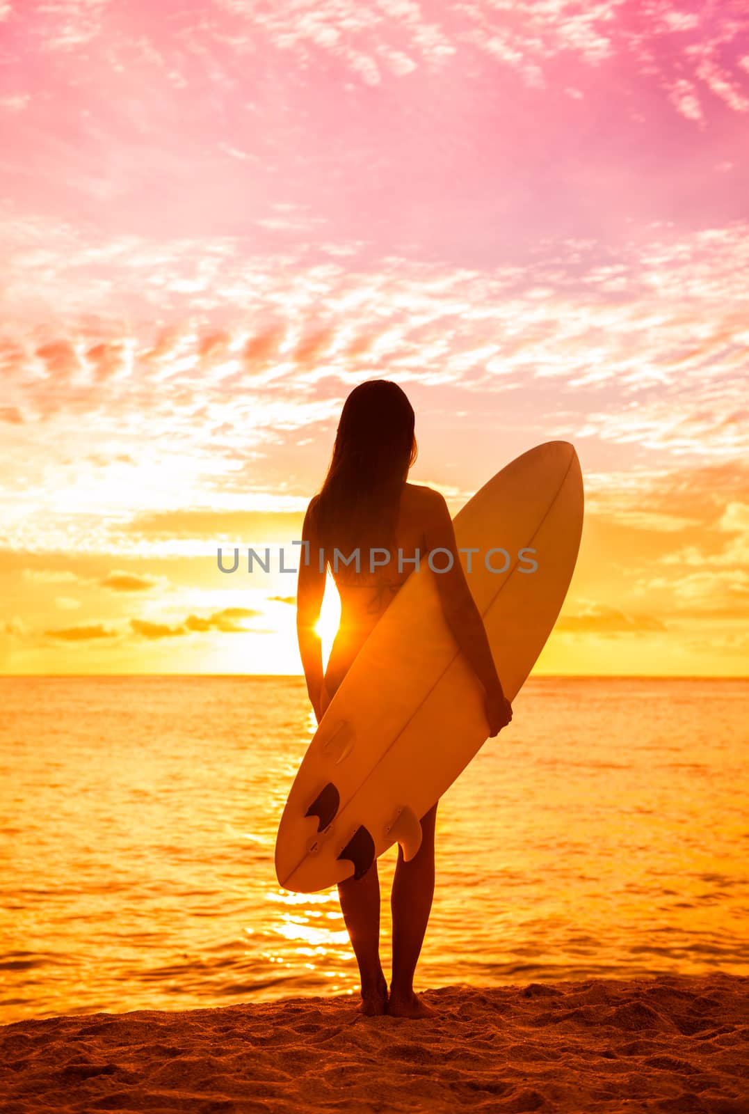 Beach sunset sexy surfer woman surfing lifestyle relaxing holding surfboard looking at ocean waves for surf. Active healthy living silhouette of sports athlete standing in colorful sky by Maridav