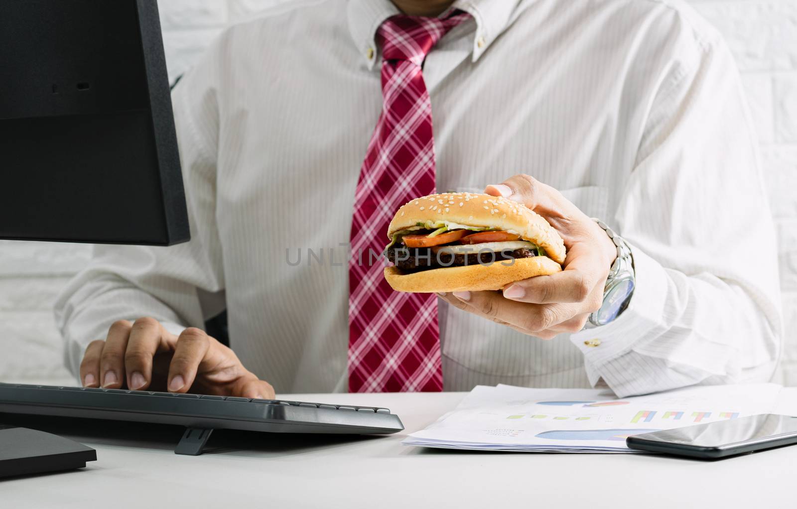 Working men do not have time to urgent eating junk food hamburger while working in office
