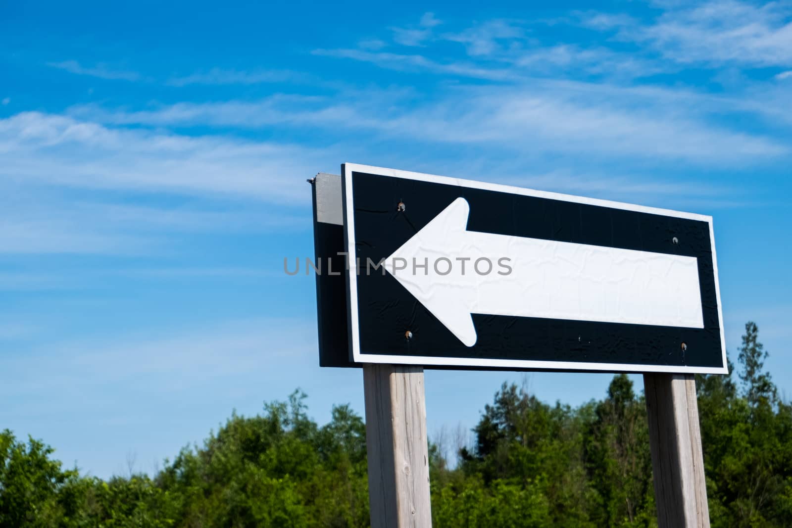 A large black-and-white one-way road sign directs traffic to the left of the frame on a sunny day.