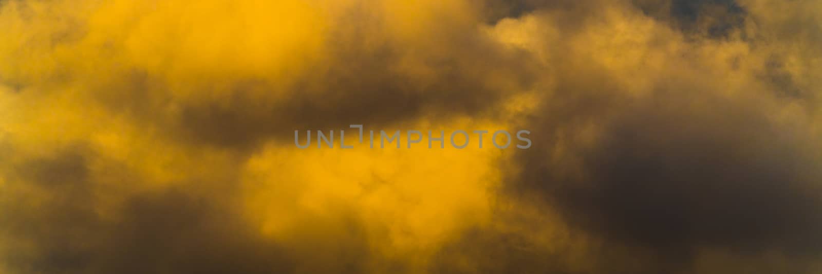 Panorama fluffy thunderstorm clouds illuminated by disappearing rays at sunset, thunderclouds floating across sunny blue sky to change season weather. Soft focus, motion blur sky landscape.