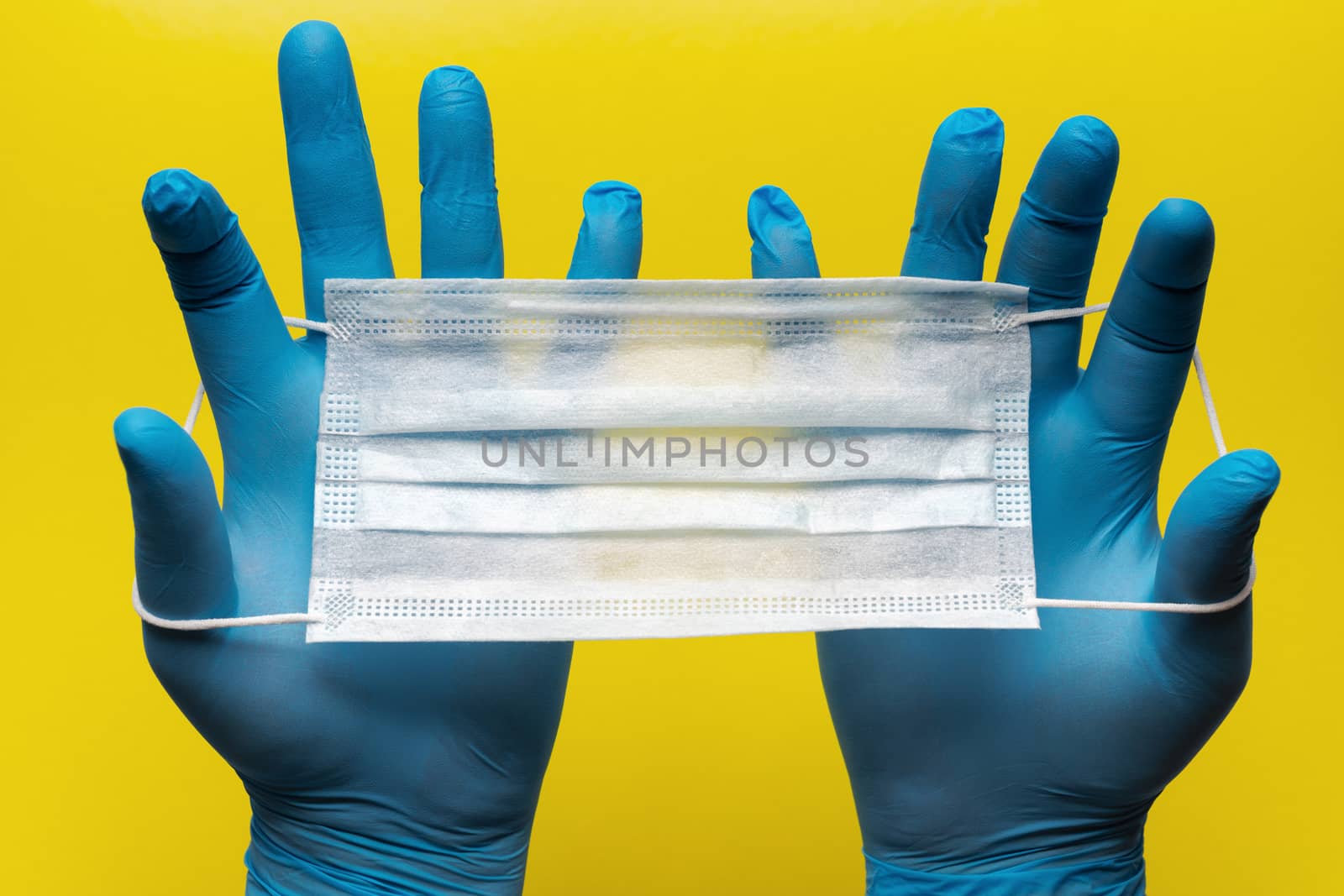 Doctor holds antivirus face mask in hands in blue medical gloves on yellow background. Pandemic insurance, airborne diseases, SARS, grippe. Medical masks for human cover nose and mouth. Concept