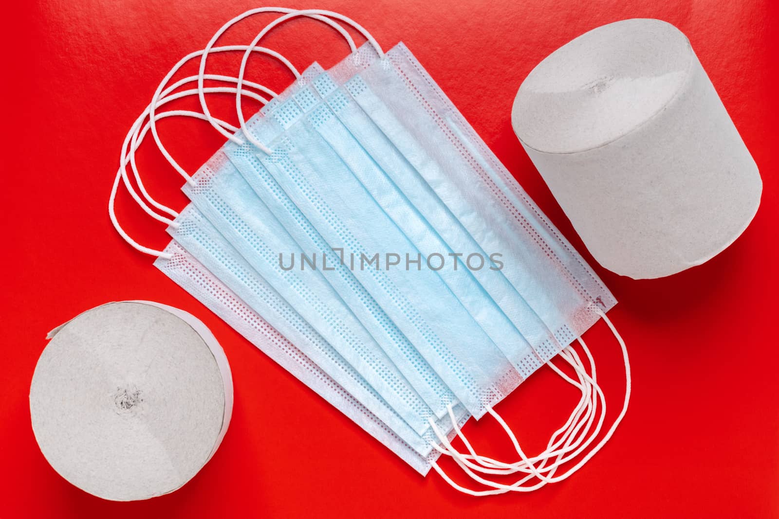 Medical surgical face masks and rolls of toilet paper on red background. World pandemic insurance, airborne diseases, coronavirus by Alexander-Piragis