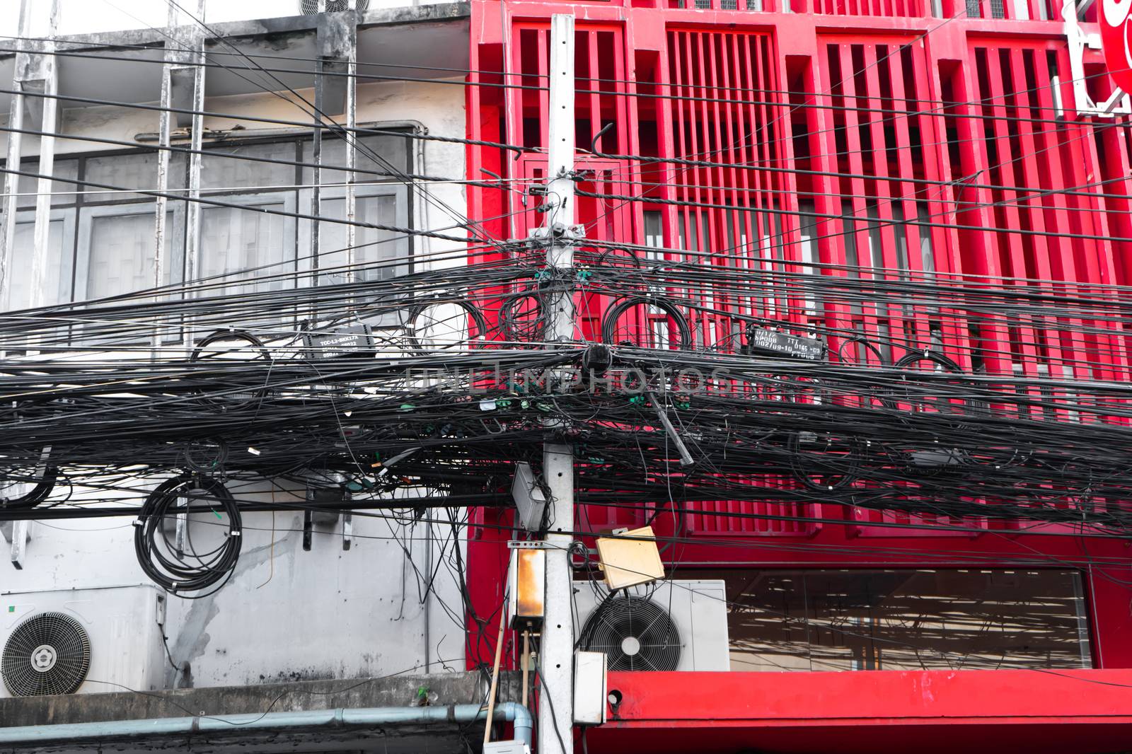 Electrical wiring post in thailand. A huge number of wires on a pole. Against the background of a red and white building.
