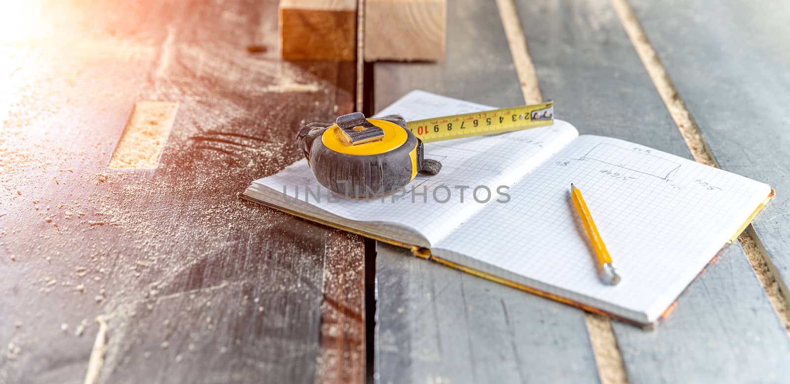 draw prepared wood products in a workbook in a joinery. tape measure, pencil and notebook on the table with chainsaw.
