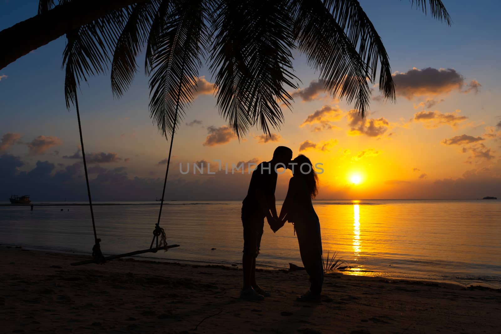 Silhouetted couple in love kisses on the beach during sunset