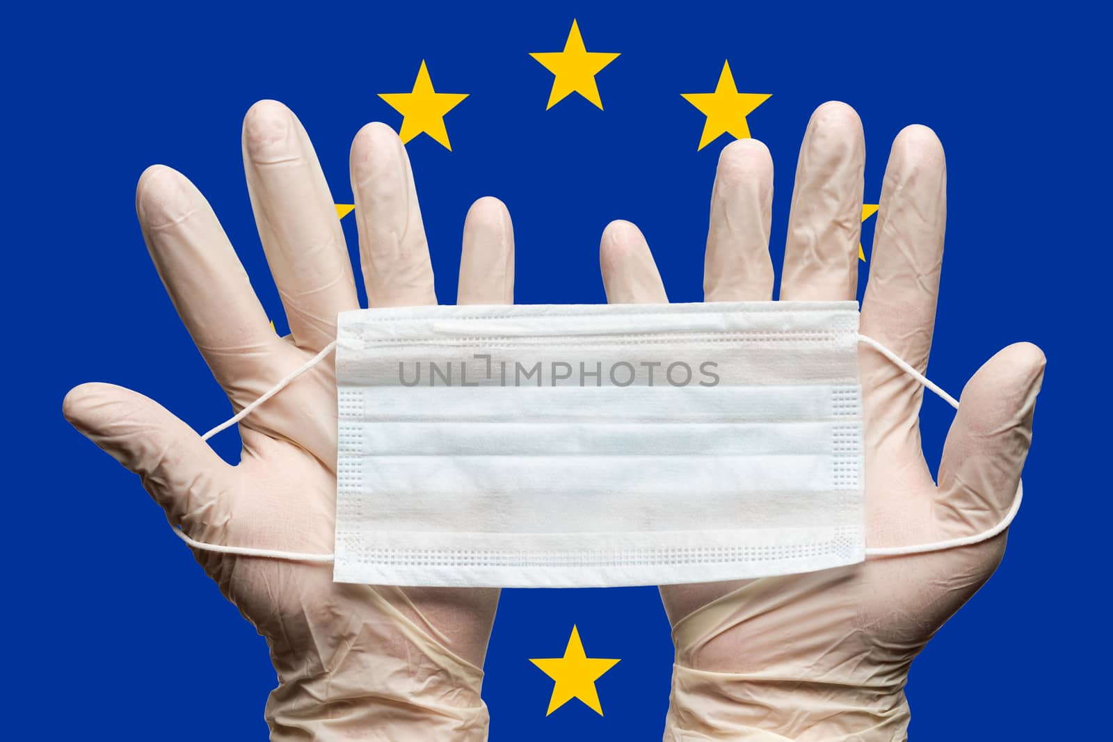 Doctor holding medical face mask in two hands in white gloves on background flag of European Union EU by Alexander-Piragis