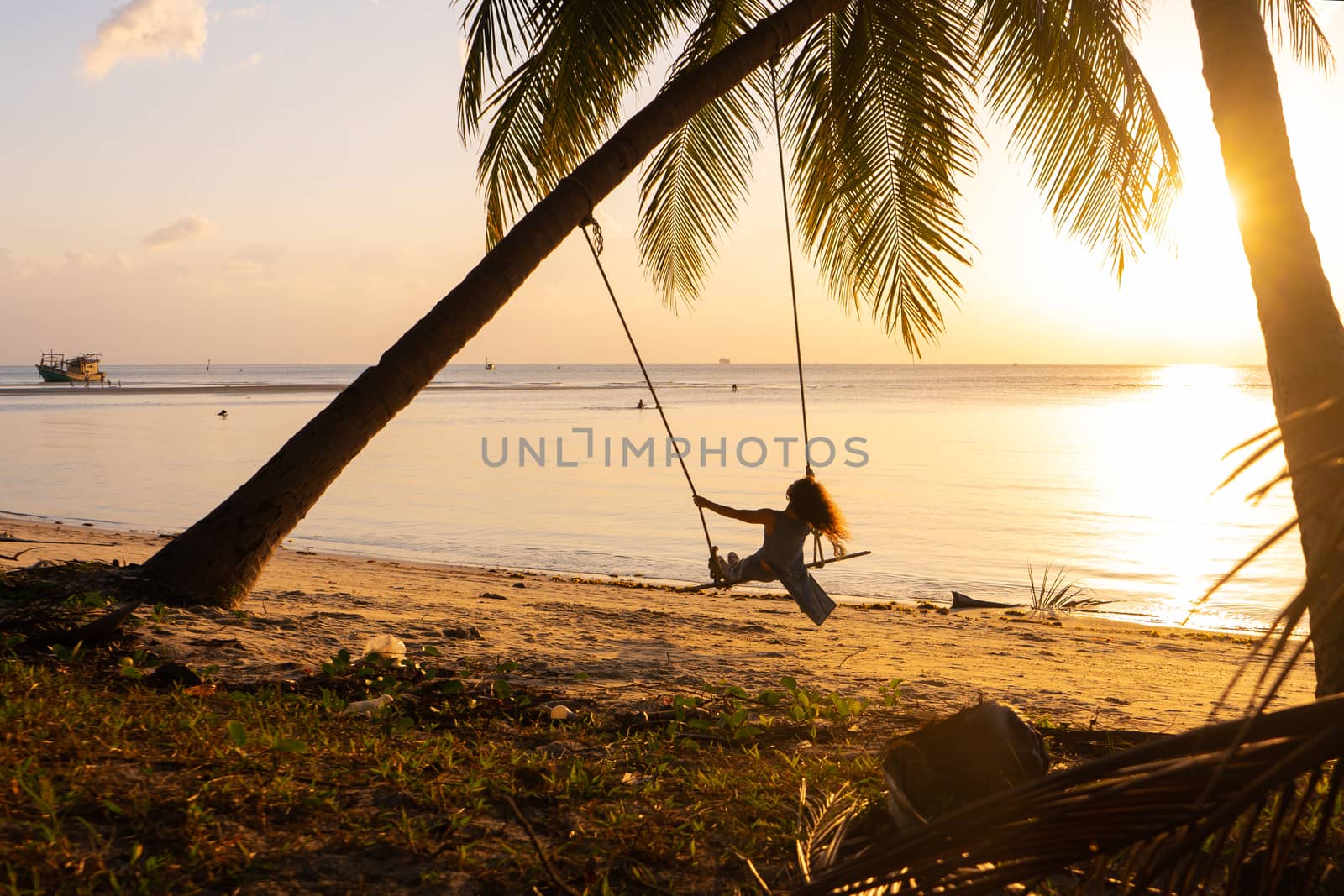The girl on the beach rides on a swing during sunset. Sunset in the tropics, enjoying nature. Swing tied to a palm tree by the ocean by Try_my_best