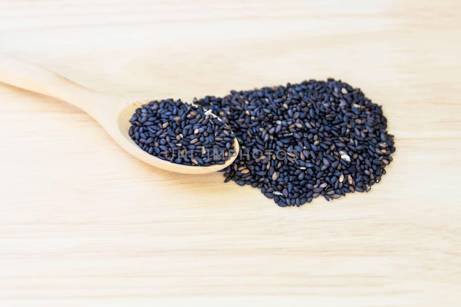 Black sesame seeds in wooden spoon pile on wood table 