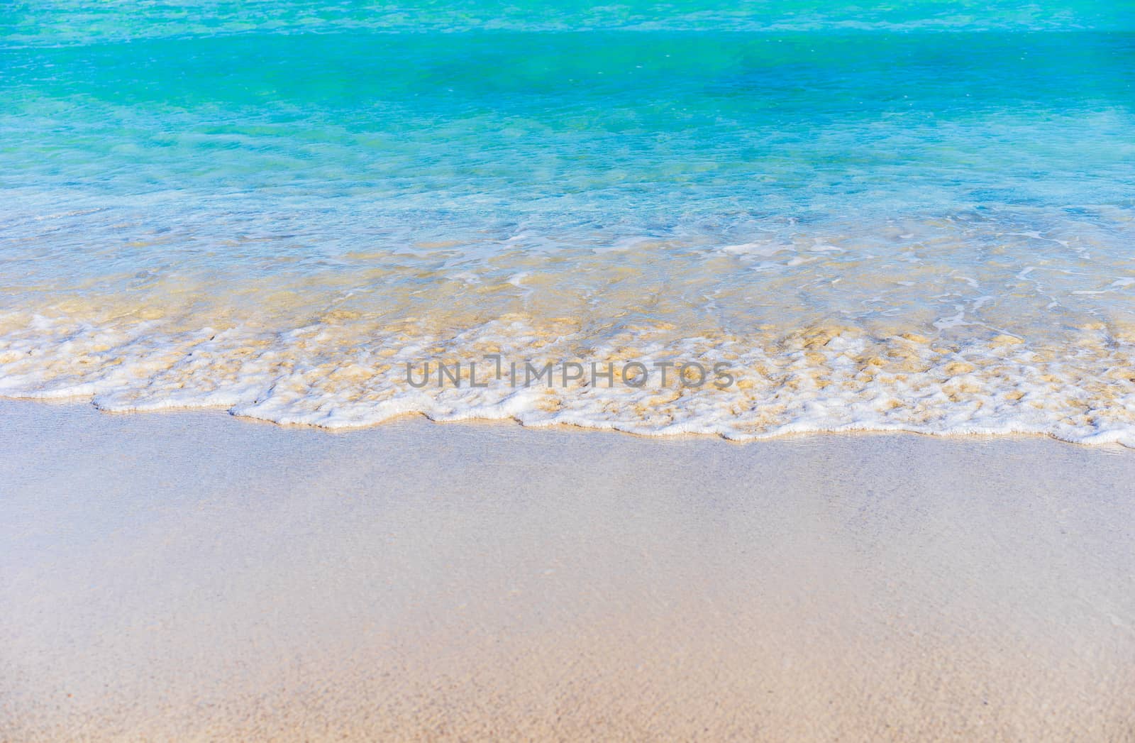 Ocean wave on sandy beach with blue sea water, background texture