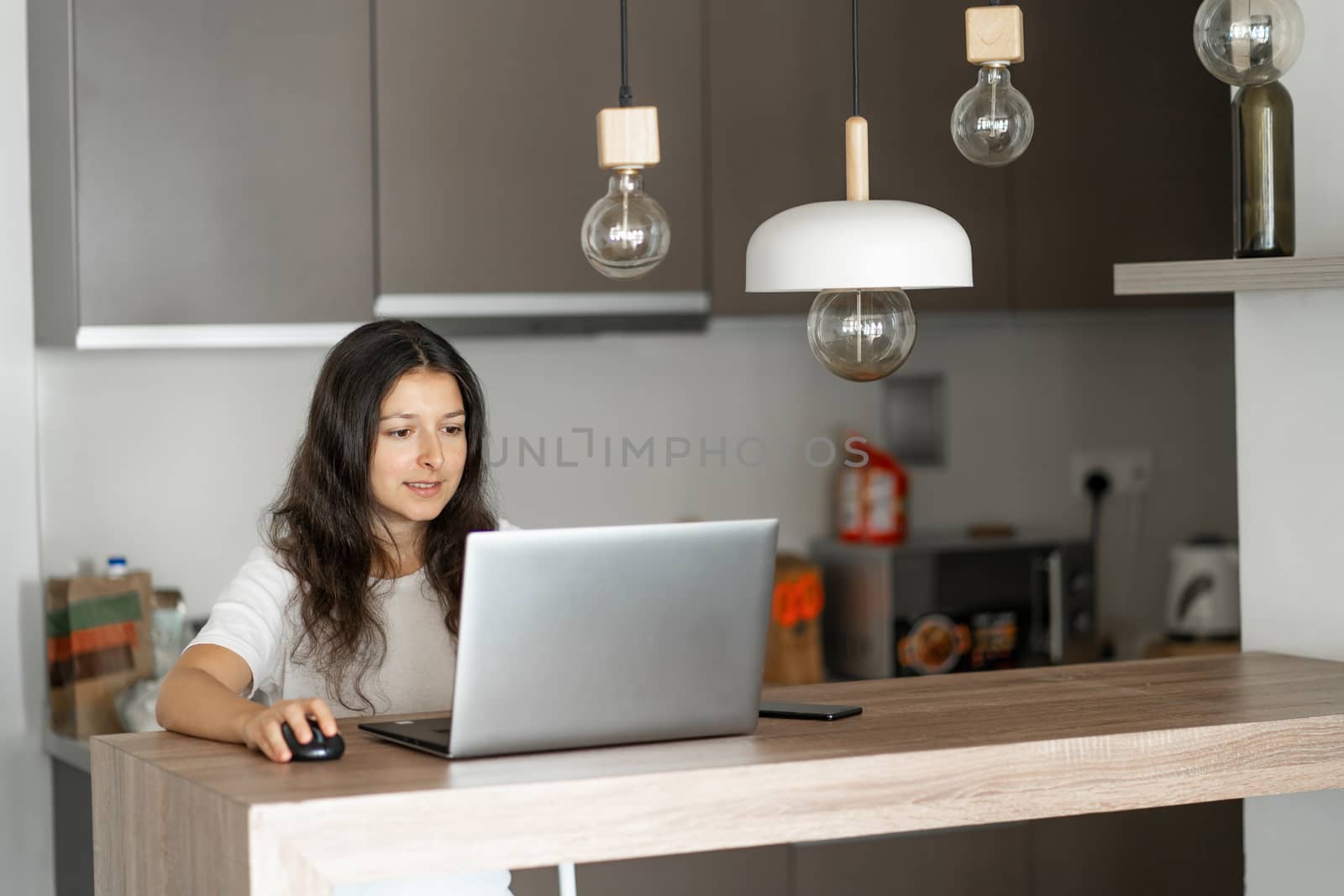 Beautiful young brunette girl working on a laptop at home in the kitchen