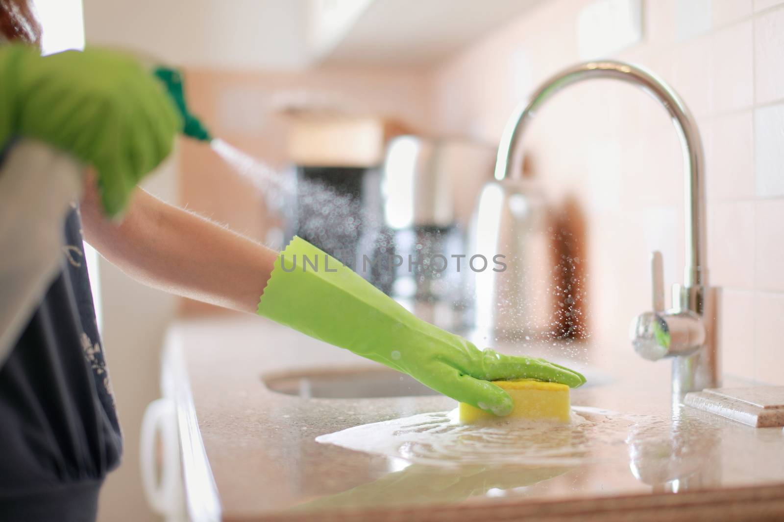 Woman cleaning and polishing the kitchen worktop with a spray detergent, housekeeping and hygiene concept. High quality photo